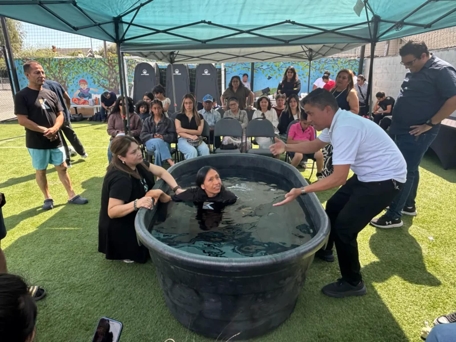 Una mujer queda sumergida en el agua sostenida por los que la bautizan