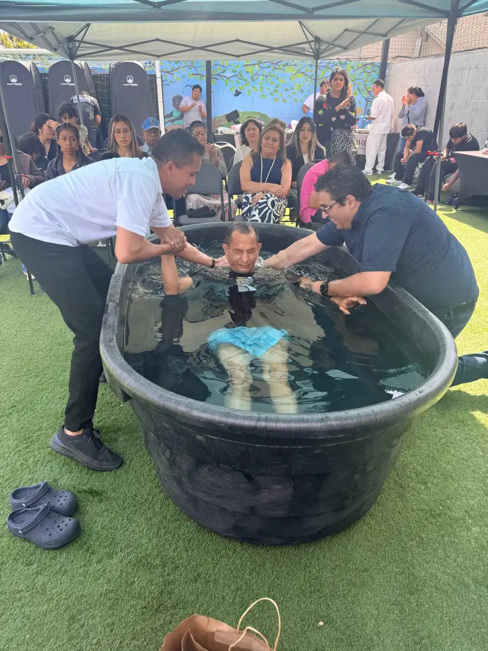 Un hombre queda sumergido en el agua sostenido por los brazos de los que lo bautizan