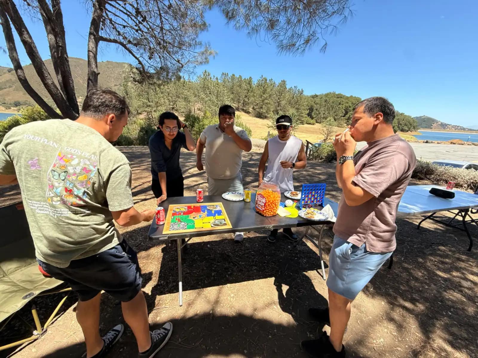 Cinco hombres alrededor de la mesa de juegos montada bajo los árboles, junto al lago