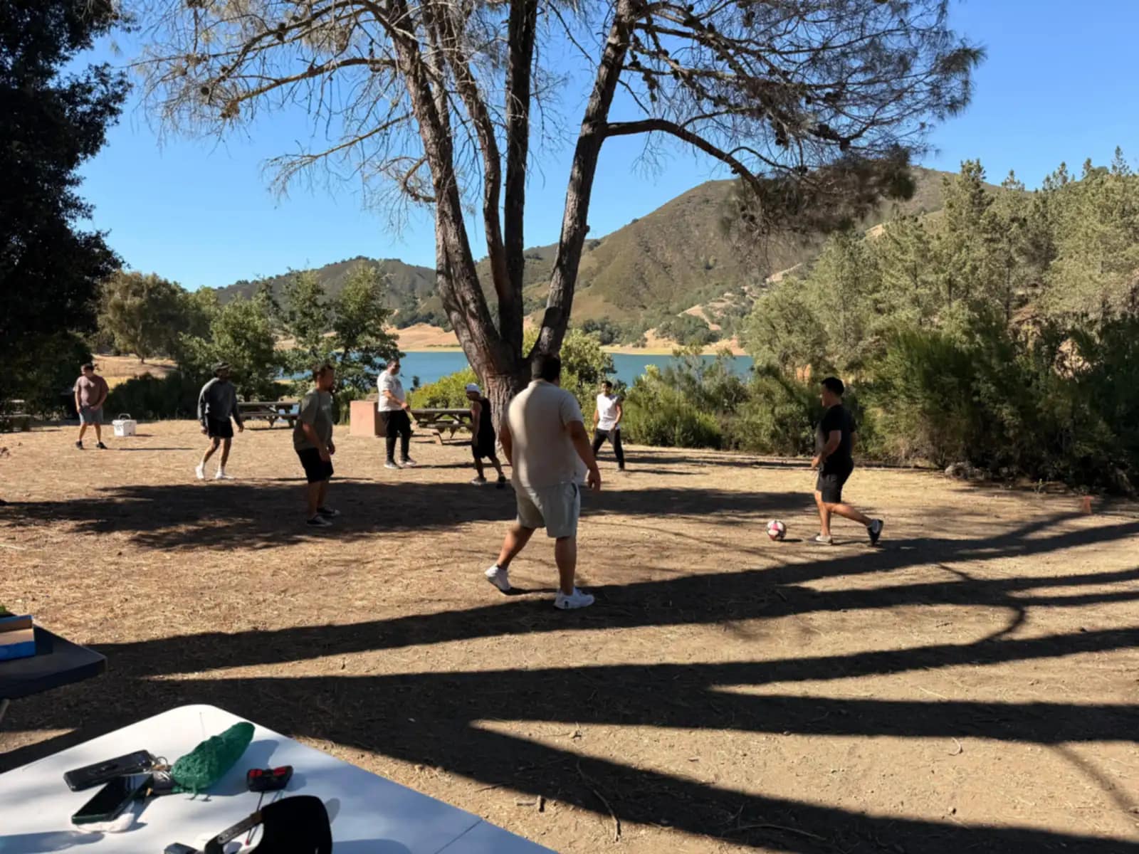 Partido de fútbol en el claro de tierra, con el lago y los cerros secos detrás