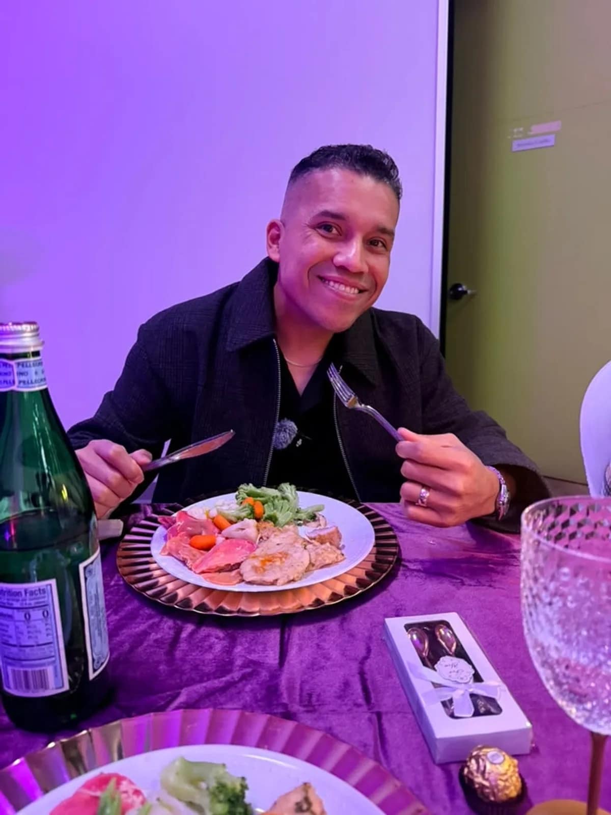 Un invitado sonríe ante su plato de la cena, con la caja de bombones sobre el mantel
