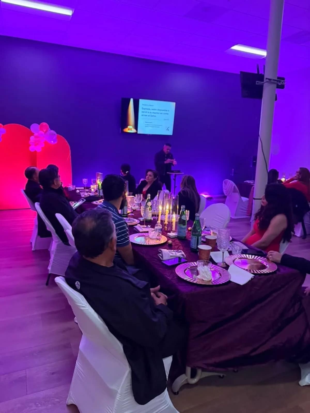 Mesa larga con velas y copas mientras el orador presenta desde el atril del fondo