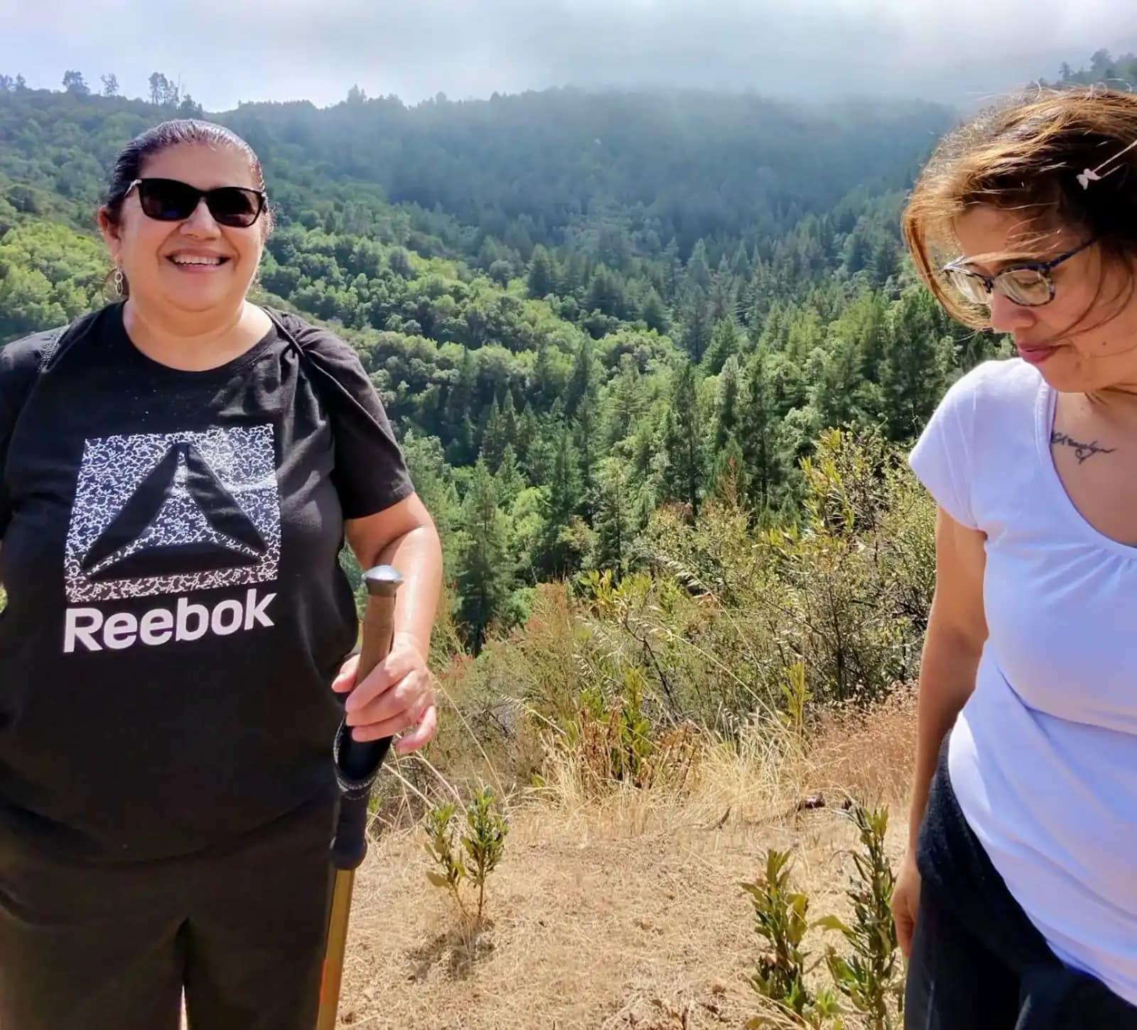 Dos mujeres de la iglesia en un mirador, con el valle cubierto de pinos y la niebla al fondo