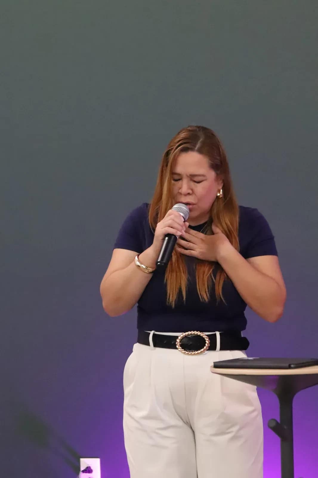 Una mujer canta con los ojos cerrados sobre el fondo morado del escenario