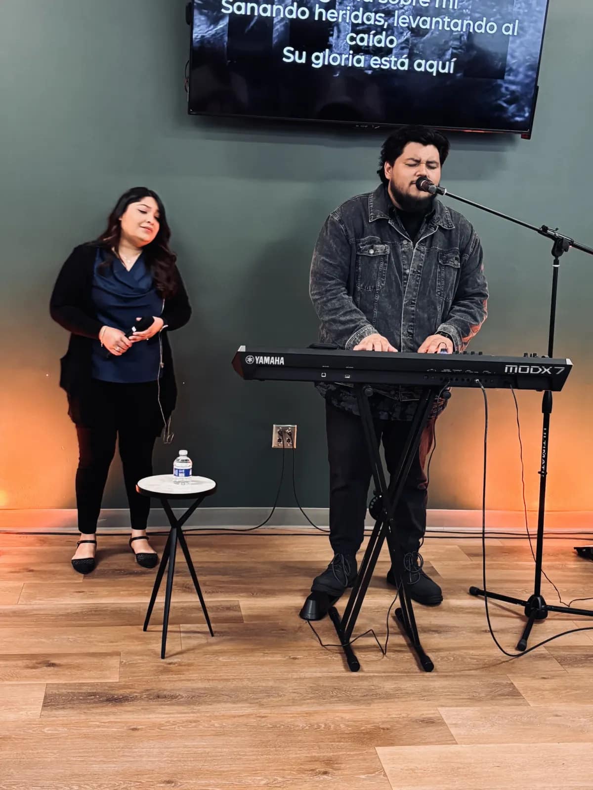 Dos jóvenes del equipo de alabanza cantan junto al teclado al inicio del servicio