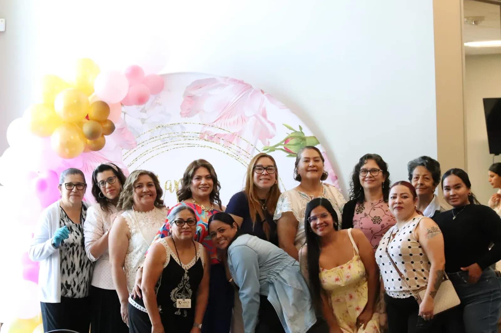 El grupo de mujeres posa ante el fondo floral de la celebración