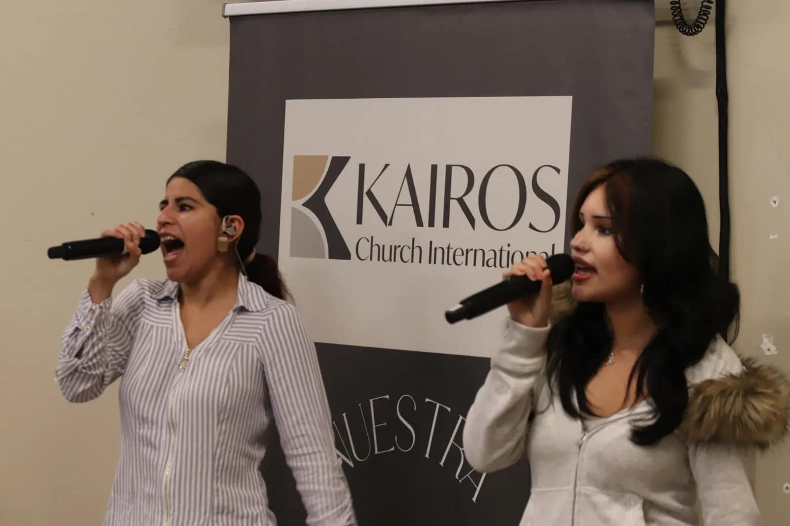 Dos cantantes del equipo de alabanza cantan ante el banner de Kairos