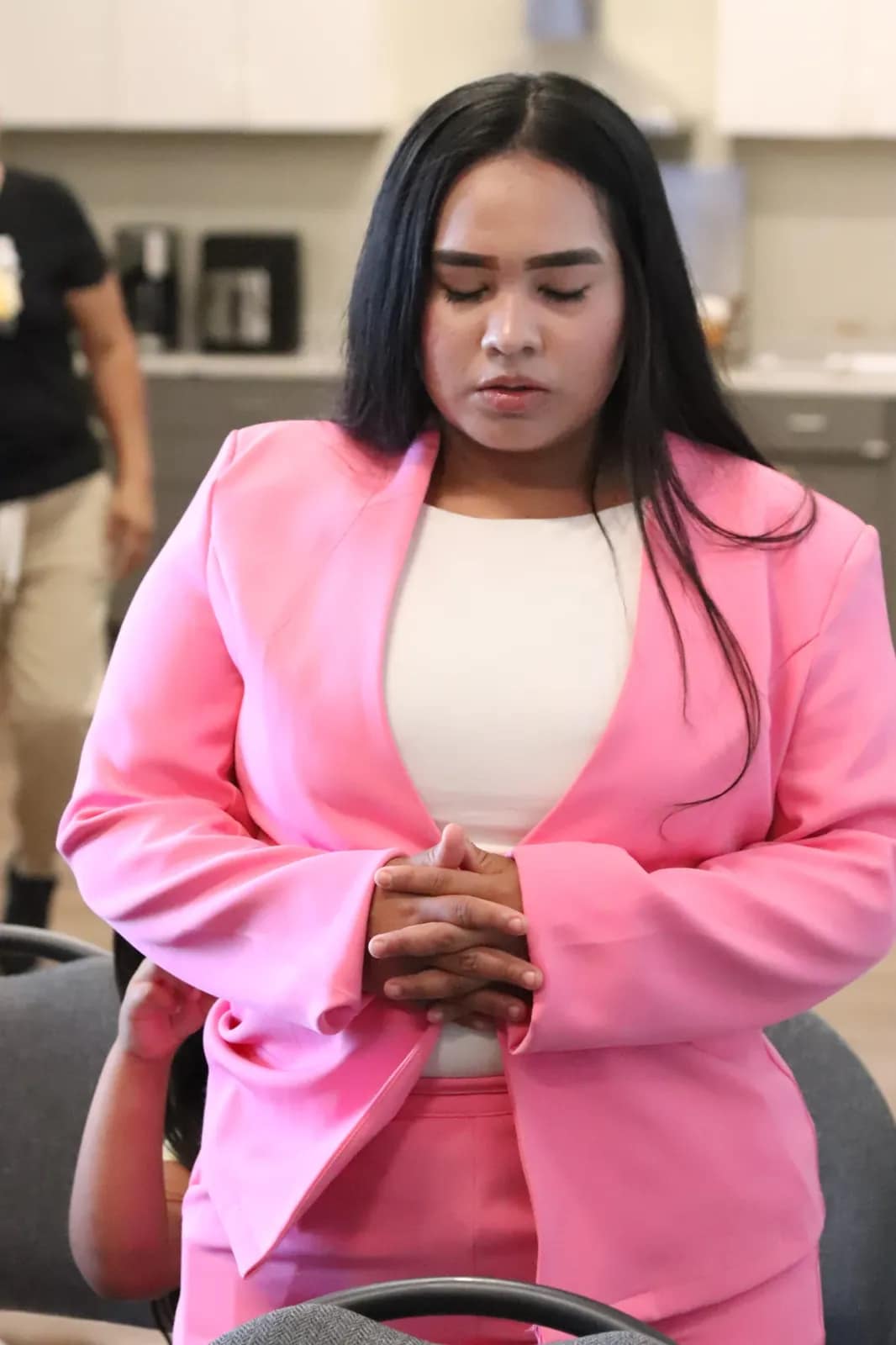 Una joven de chaqueta rosa ora en silencio con las manos juntas