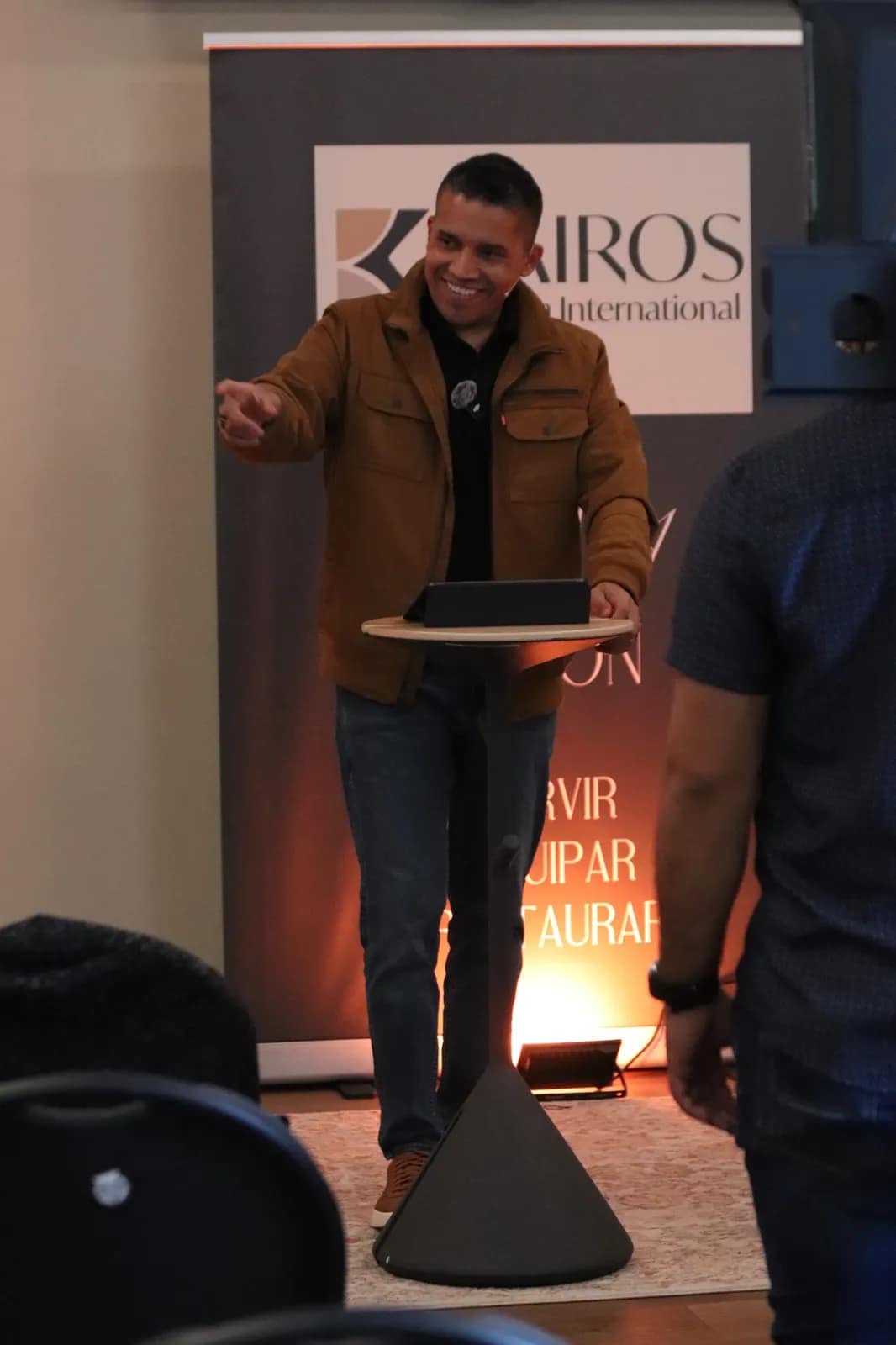 El predicador habla junto al banner de Kairos al fondo del salón