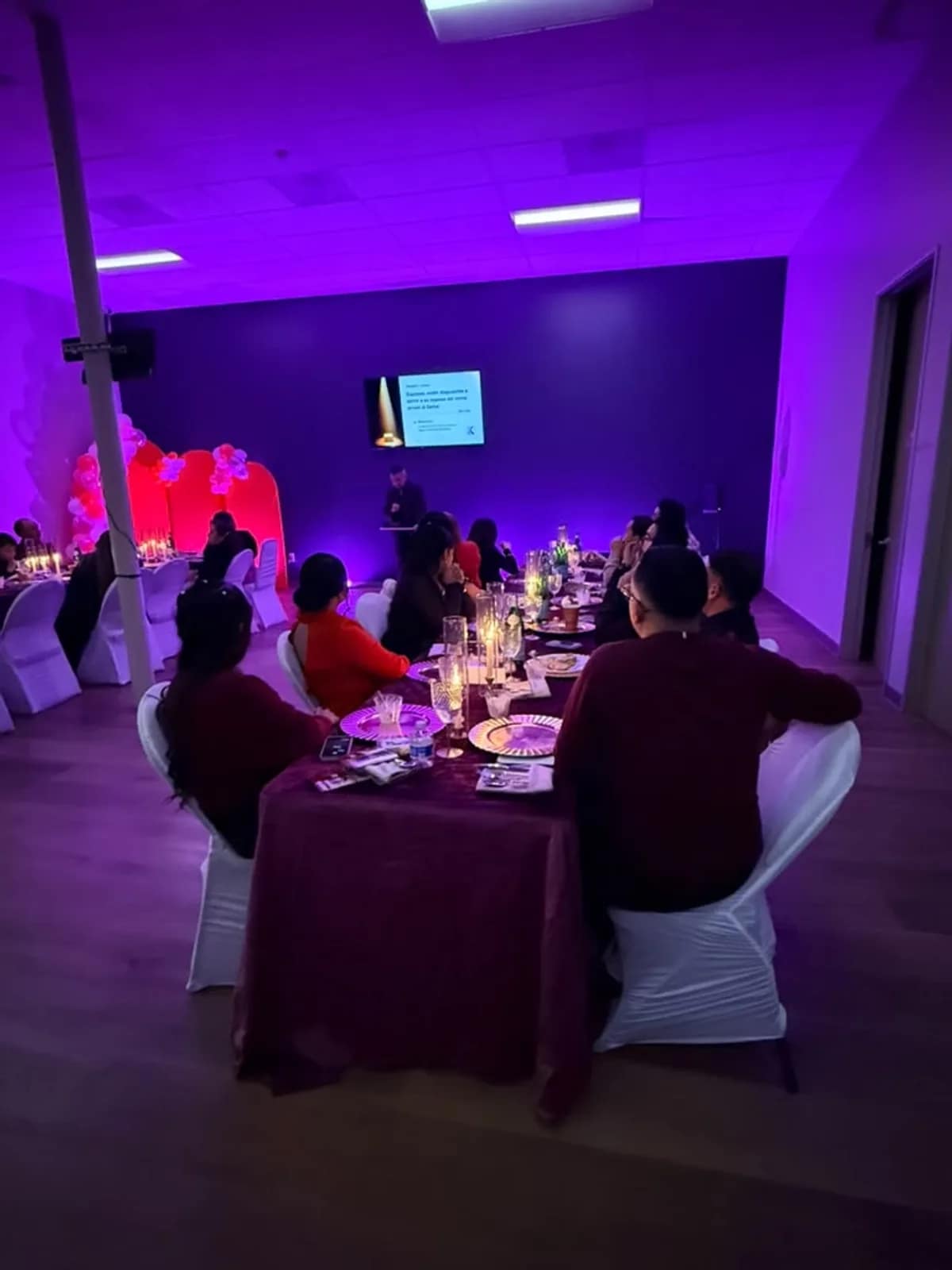 El salón con luz morada, mesas redondas con velas y un arco de globos rojos al fondo